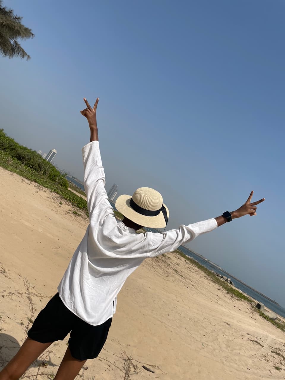 Timonwa at the beach with her back to the camera and her hands in the air showing the peace sign